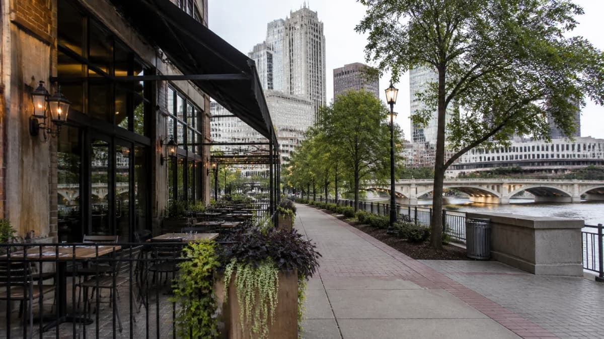 AI-generated illustration of an anonymous restaurant patio beside a riverfront path.