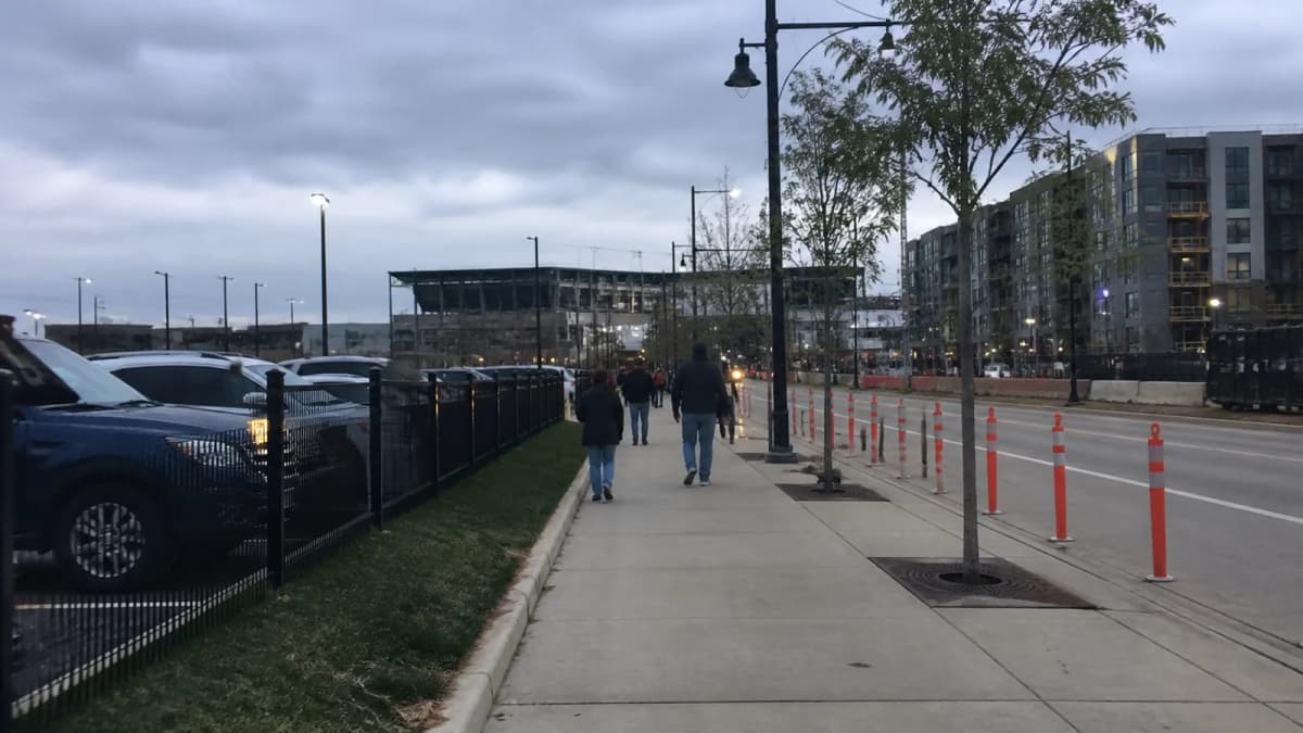 AI-generated illustration of a sidewalk between parking and apartments near a stadium-like structure.