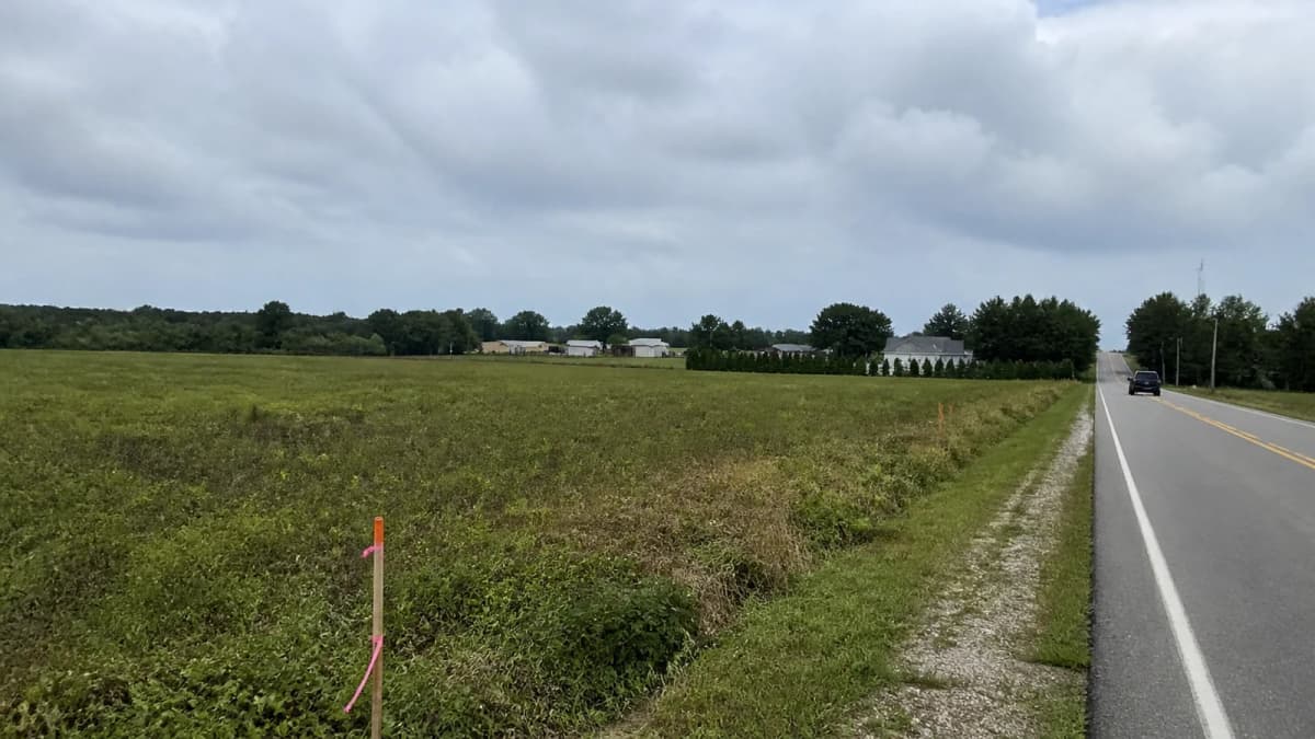 AI-generated illustration of an open field beside a road, survey stakes and distant houses.