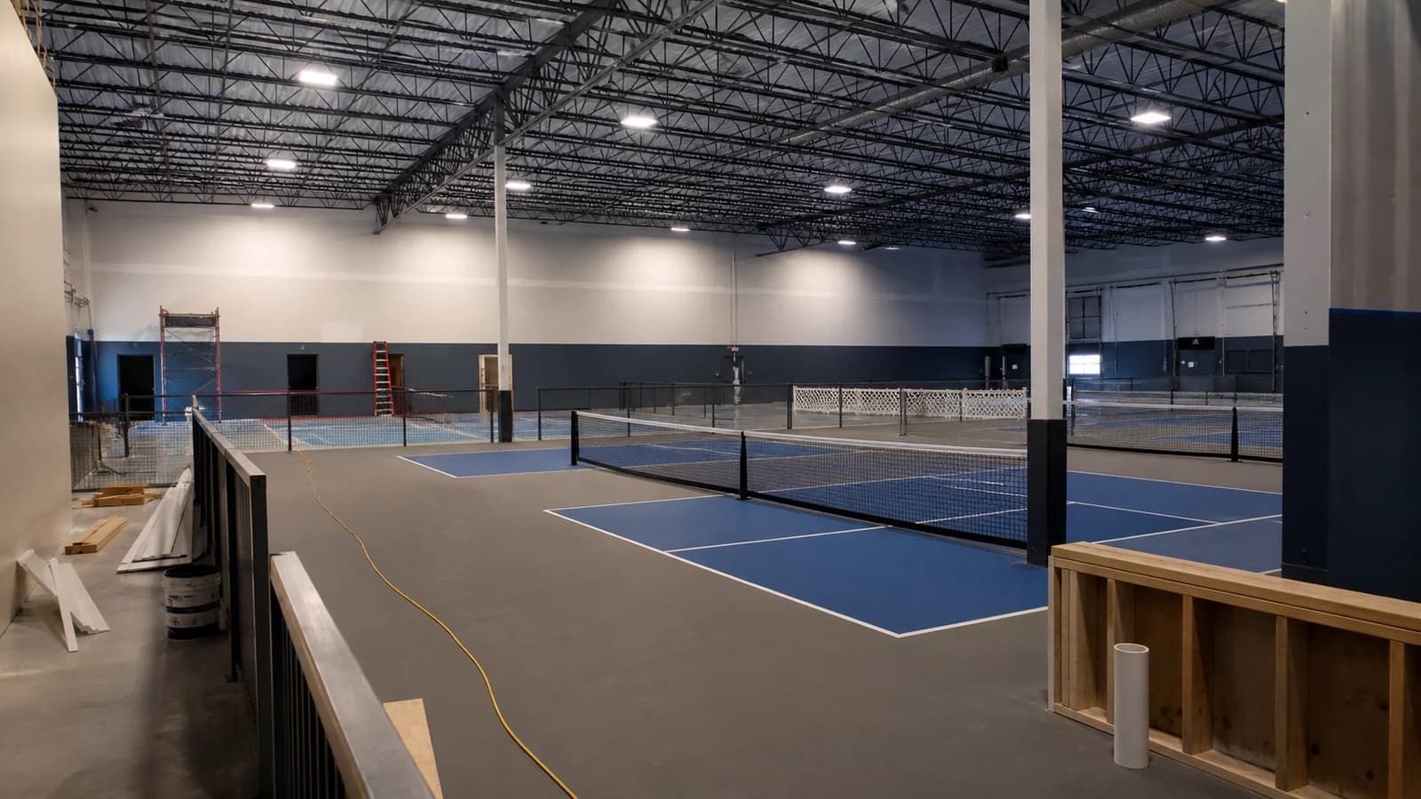 Illustration of a bright indoor facility with multiple pickleball courts and a mezzanine viewing area.