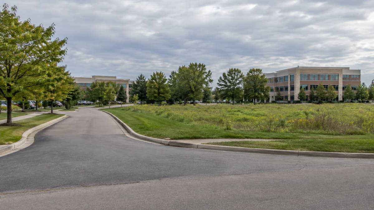 AI-generated illustration of an office-campus road beside a grassy parcel and distant office buildings.