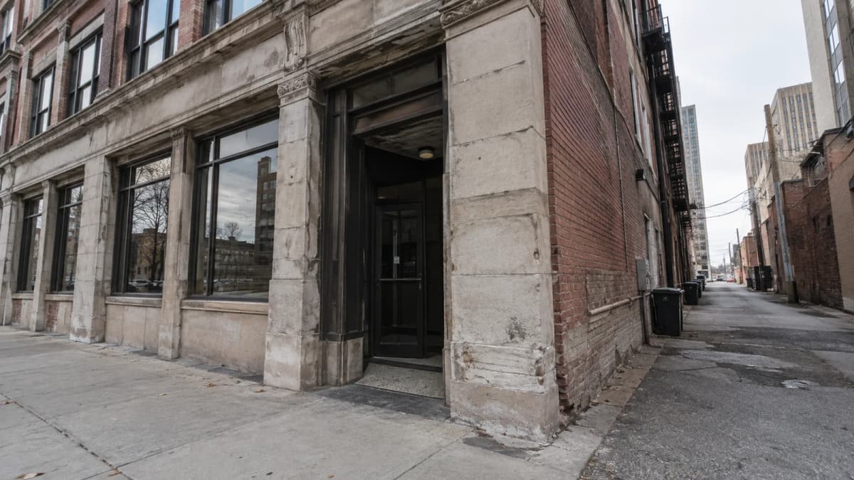 AI-generated illustration of a weathered brick building with stone trim and a narrow side alley.